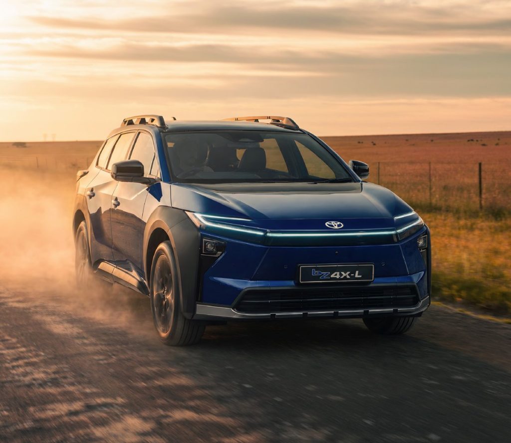 Blue Toyota bZ4X Touring driving on a gravel farm road at sunset